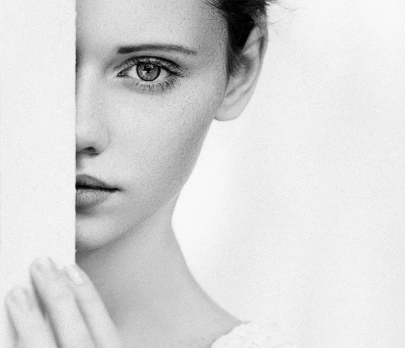 Schwarz-Weiß-Porträt: Gesicht einer Frau, zur Hälfte hinter einer Wand